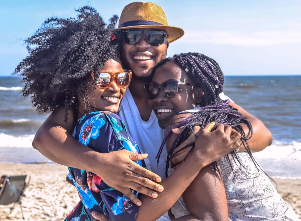 Two women and a man smiling happily. The two women in a friendly hug in the mans arms.