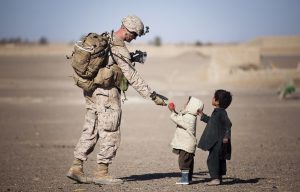 A soldier reaching out to two small kids on a road