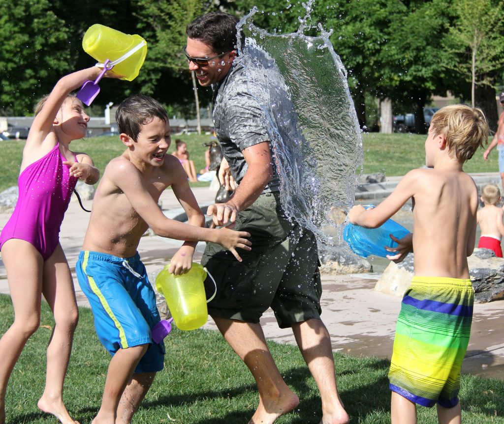 Three children and on male adult in a water fight outside in a park