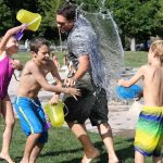Three children and on male adult in a water fight outside in a park
