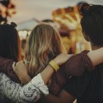 Three friends holding each others shoulders. Picture from their back.